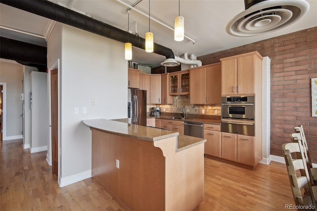 kitchen featuring sink, appliances with stainless steel finishes, kitchen peninsula, decorative light fixtures, and dark stone counters