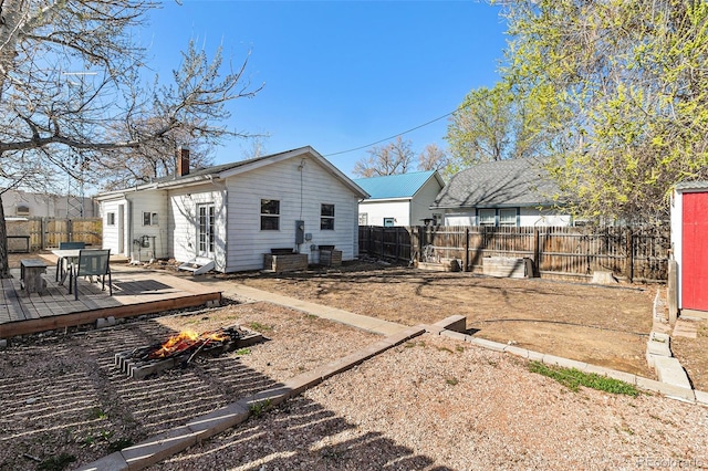 rear view of property featuring a deck, a fenced backyard, a chimney, an outdoor fire pit, and an outbuilding