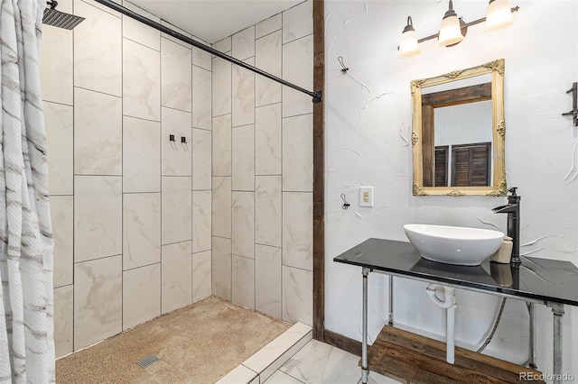 bathroom with a sink, marble finish floor, and tiled shower
