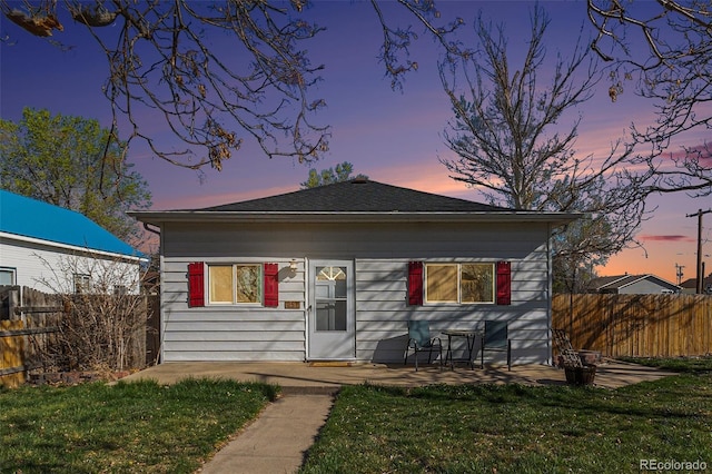 bungalow-style home featuring a patio, a shingled roof, a front lawn, and fence