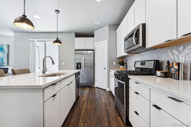 kitchen with pendant lighting, sink, stainless steel appliances, white cabinets, and a center island with sink