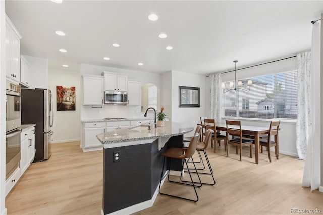 60 Stewart Way, Erie, CO 80516 - kitchen featuring appliances with stainless steel finishes, a sink, an island with sink, white cabinets, and backsplash