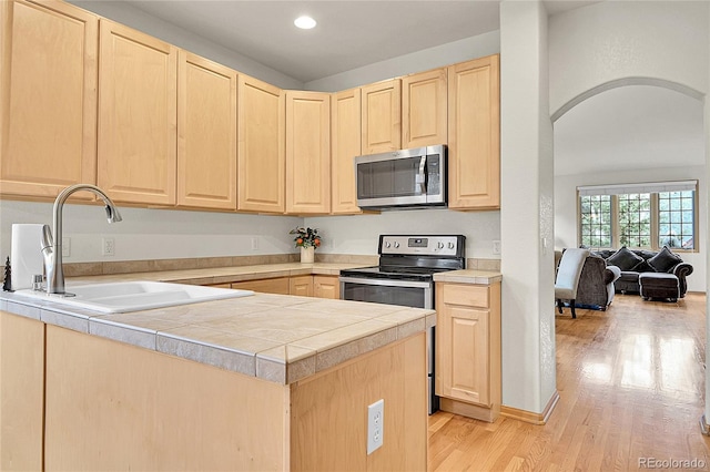 31139 Tahoe Ct, Evergreen, CO 80439 - kitchen with light brown cabinetry, stainless steel appliances, a sink, arched walkways, and light wood finished floors