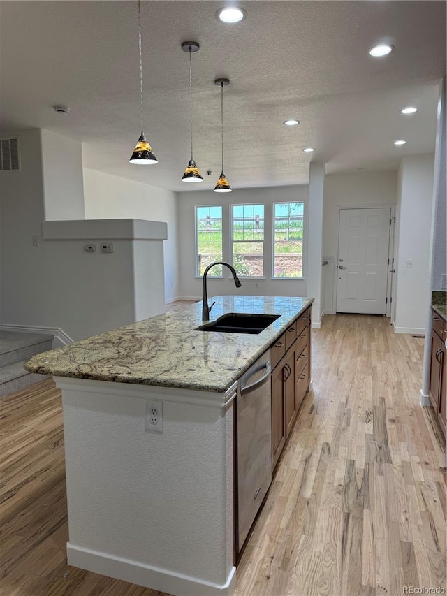 12317 W Gould Ave, Littleton, CO 80127 - kitchen featuring stainless steel dishwasher, light wood-style floors, light stone countertops, a center island with sink, and recessed lighting