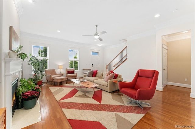 living area with a premium fireplace, wood finished floors, ornamental molding, and stairs