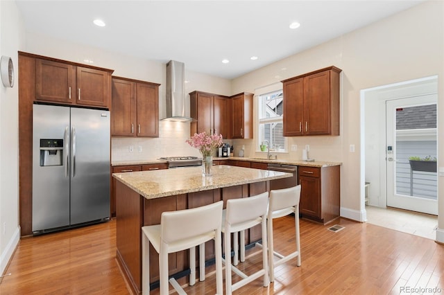 kitchen featuring light wood-style flooring, a sink, decorative backsplash, wall chimney exhaust hood, and stainless steel appliances