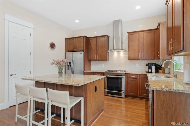 kitchen featuring a center island, a sink, wall chimney exhaust hood, stainless steel appliances, and light wood-style floors
