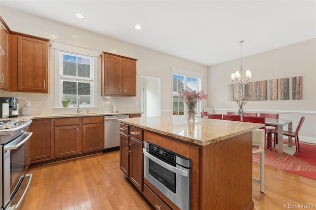 kitchen with a sink, stainless steel appliances, brown cabinets, a kitchen breakfast bar, and light wood-style flooring