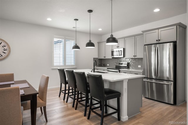 9157 Rio Lado St, Littleton, CO 80125 - kitchen featuring appliances with stainless steel finishes, an island with sink, backsplash, light countertops, and a kitchen bar