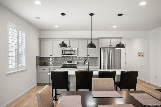 9157 Rio Lado St, Littleton, CO 80125 - kitchen featuring stainless steel appliances, gray cabinetry, decorative backsplash, a kitchen island with sink, and light countertops