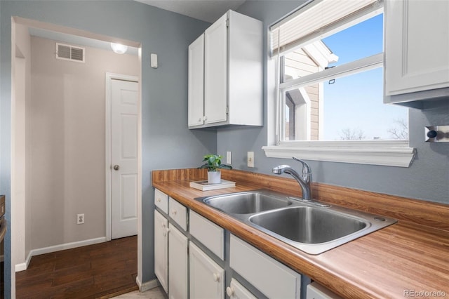 kitchen featuring visible vents, a sink, wood finished floors, and white cabinets