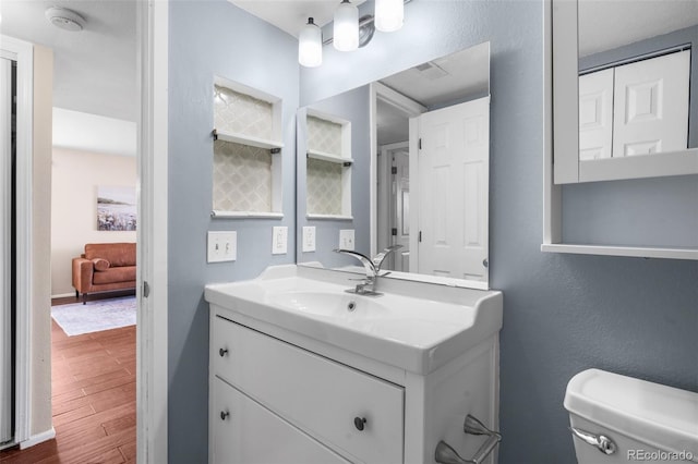 bathroom with toilet, visible vents, wood finished floors, and vanity