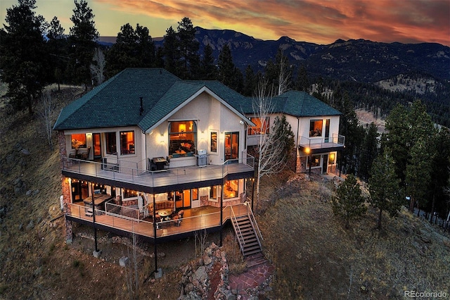 back of house at dusk featuring a balcony, stairway, and a mountain view