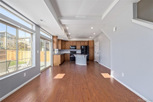 kitchen with a kitchen breakfast bar, dark hardwood / wood-style flooring, backsplash, a kitchen island, and black appliances