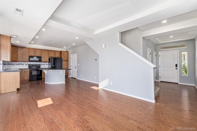 kitchen with a center island, tasteful backsplash, a raised ceiling, dark hardwood / wood-style floors, and black appliances