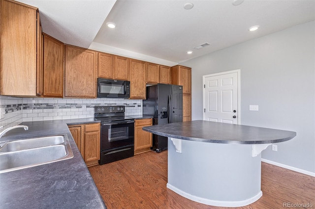 kitchen featuring sink, dark hardwood / wood-style floors, backsplash, a kitchen bar, and black appliances