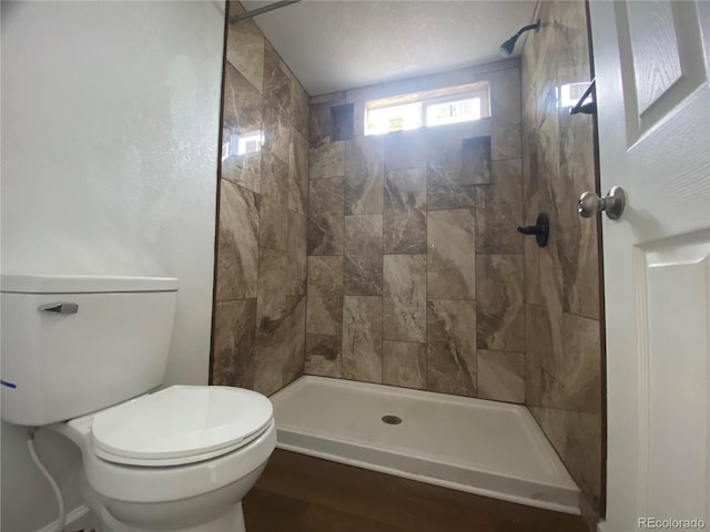 bathroom featuring hardwood / wood-style floors, toilet, and tiled shower