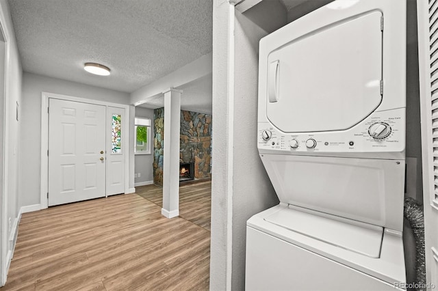 2678 S Xanadu Way Unit C, Aurora, CO 80014 - laundry room with stacked washing machine and dryer, light wood-style flooring, a stone fireplace, and a textured ceiling