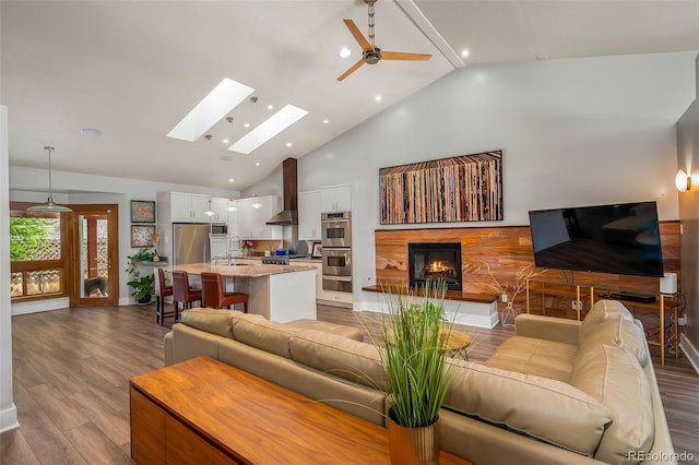 living room with wood finished floors, a ceiling fan, high vaulted ceiling, a lit fireplace, and a skylight