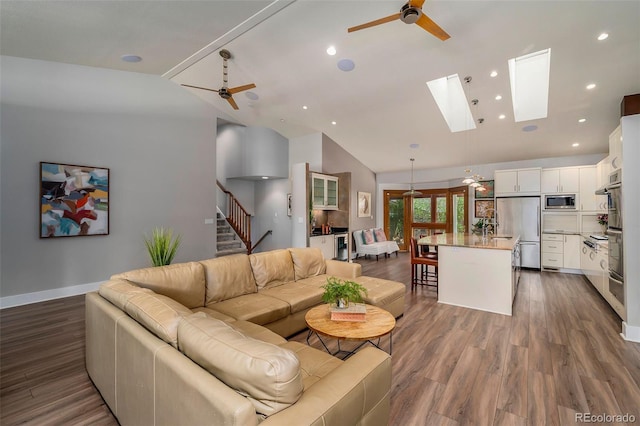 living area featuring vaulted ceiling, ceiling fan, stairway, wood finished floors, and baseboards