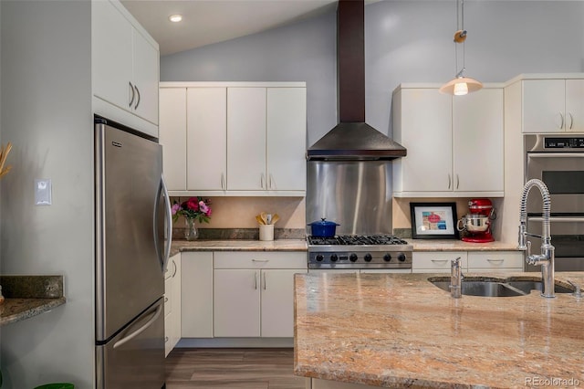 kitchen featuring freestanding refrigerator, a sink, wall chimney range hood, range, and pendant lighting