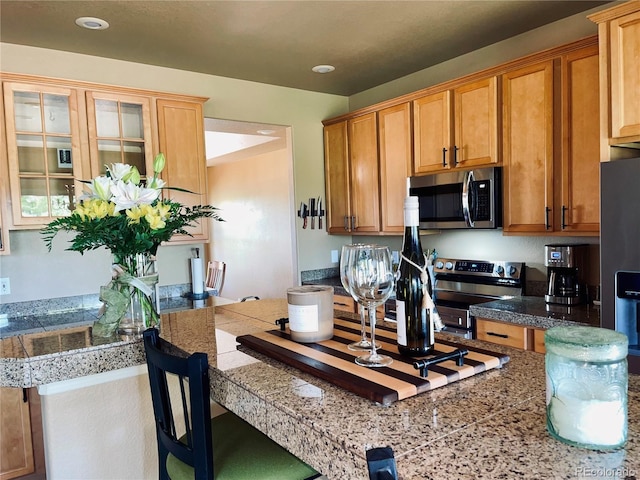 690 Antelope Dr, Bennett, CO 80102 - kitchen featuring stainless steel appliances, tile counters, glass insert cabinets, a breakfast bar, and recessed lighting