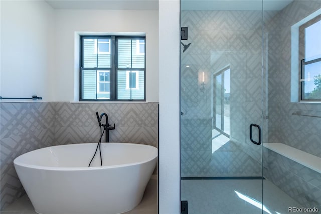 full bathroom featuring a shower stall, tile walls, a soaking tub, and plenty of natural light