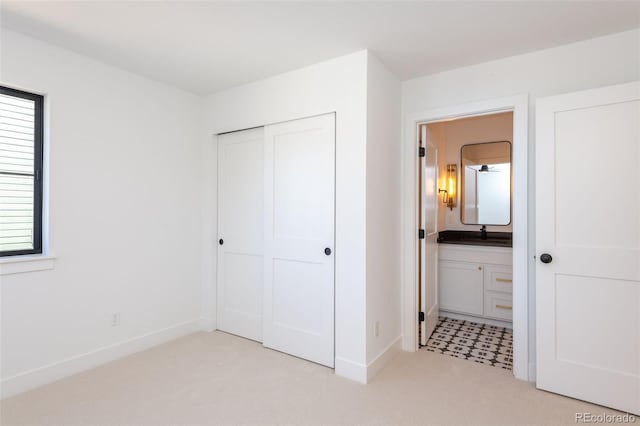 unfurnished bedroom with a sink, ensuite bathroom, a closet, light carpet, and baseboards
