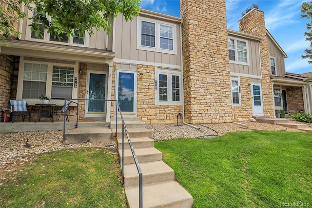 9615 W Chatfield Ave Unit C, Littleton, CO 80128 - view of front facade featuring board and batten siding, stone siding, a front lawn, and a chimney