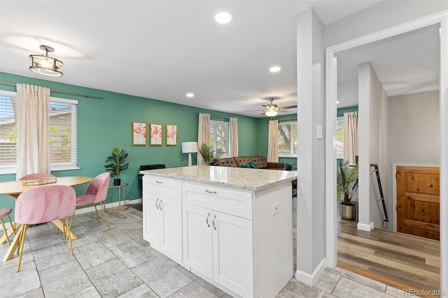 8506 Eaton St, Arvada, CO 80003 - kitchen with recessed lighting, white cabinetry, light stone countertops, a kitchen island, and a ceiling fan