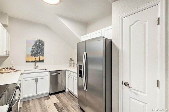 kitchen with sink, stainless steel appliances, light hardwood / wood-style floors, vaulted ceiling, and white cabinets