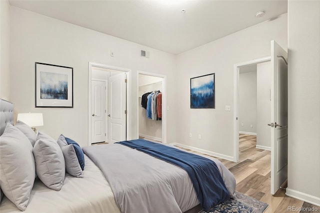 bedroom featuring a walk in closet, light hardwood / wood-style flooring, and a closet