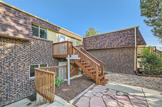 2241 Dexter Dr Unit 3, Longmont, CO 80501 - view of exterior entry featuring brick siding, a wooden deck, mansard roof, and roof with shingles