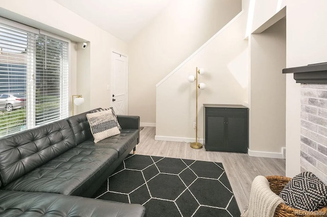 living room featuring light hardwood / wood-style floors, a stone fireplace, a healthy amount of sunlight, and vaulted ceiling