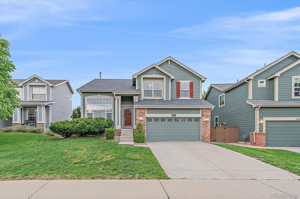 9869 Burberry Way, Highlands Ranch, CO 80129 - view of front of home featuring driveway, an attached garage, a front yard, and brick siding