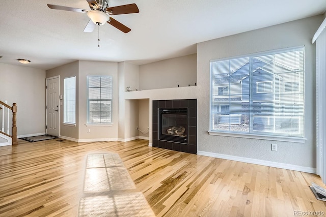 unfurnished living room featuring a fireplace, light wood-type flooring, ceiling fan, and a healthy amount of sunlight