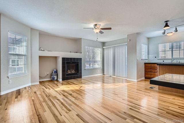 living room featuring a tile fireplace, light hardwood / wood-style floors, plenty of natural light, and ceiling fan