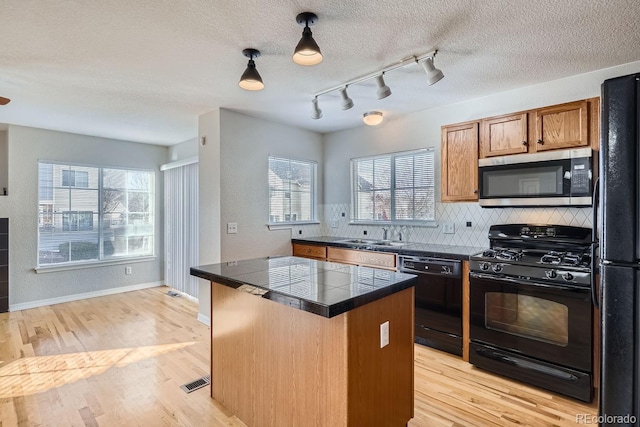 kitchen with a center island, light hardwood / wood-style flooring, a healthy amount of sunlight, and black appliances