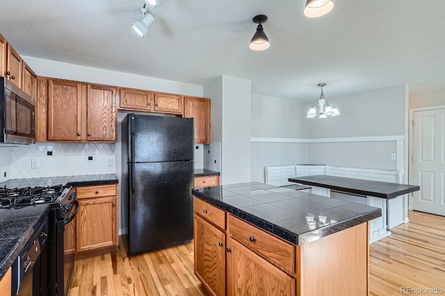 kitchen featuring black appliances, a chandelier, light hardwood / wood-style floors, a kitchen island, and hanging light fixtures