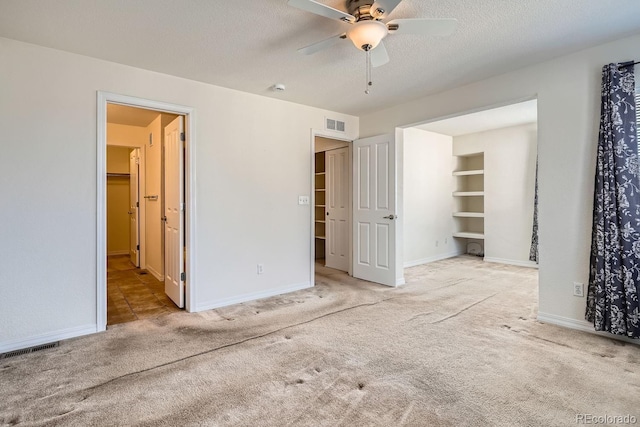 unfurnished bedroom featuring a walk in closet, ceiling fan, light colored carpet, and a textured ceiling