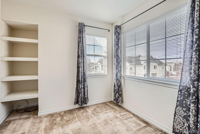 spare room featuring plenty of natural light, light colored carpet, and built in features