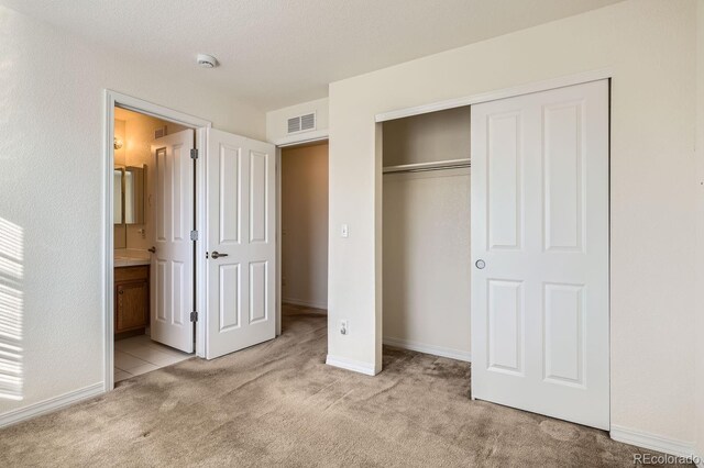 unfurnished bedroom with ensuite bathroom, light carpet, and a closet