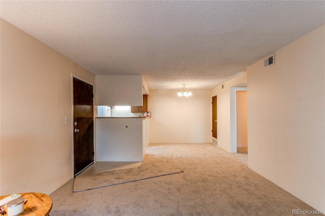 spare room with an inviting chandelier, light carpet, and a textured ceiling