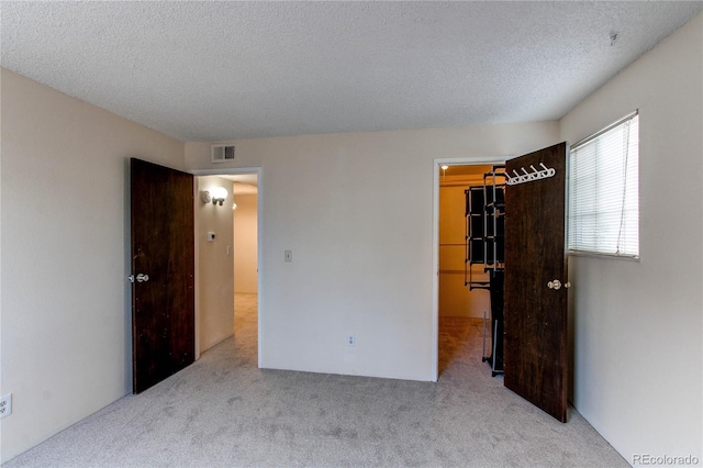 unfurnished bedroom featuring light carpet, a walk in closet, a closet, and a textured ceiling