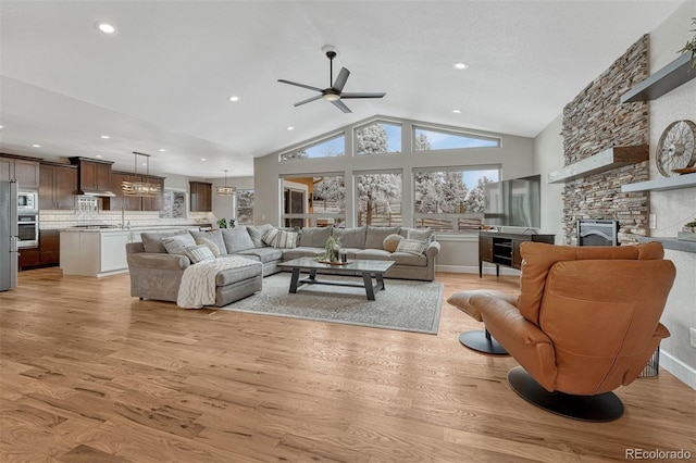 living room with ceiling fan, high vaulted ceiling, a fireplace, baseboards, and light wood-style floors