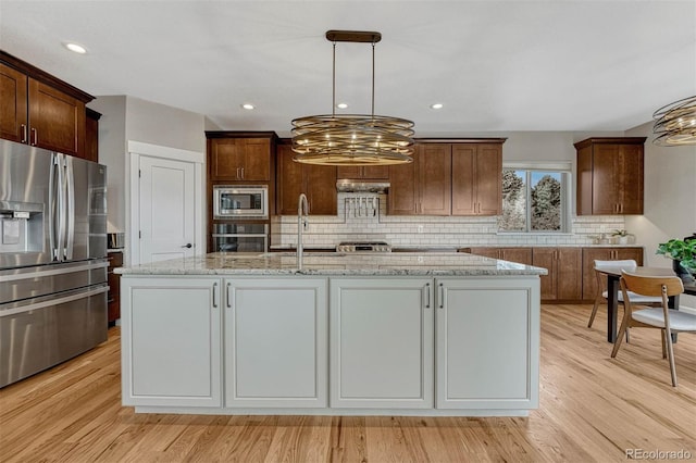 kitchen featuring light wood finished floors, backsplash, light stone countertops, stainless steel appliances, and a sink