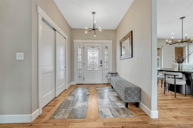 foyer featuring baseboards, a textured wall, light wood-type flooring, and a notable chandelier