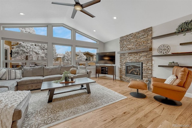 living area with high vaulted ceiling, a wealth of natural light, a fireplace, and wood finished floors