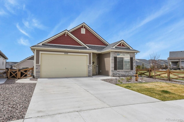 craftsman-style house with concrete driveway, fence, and stone siding