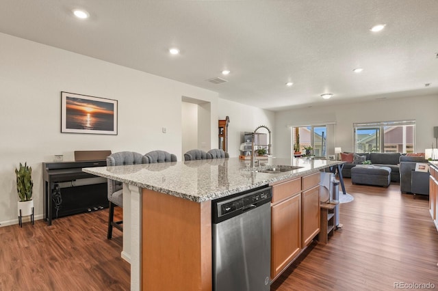 kitchen with dark wood-style floors, stainless steel dishwasher, a sink, a kitchen bar, and open floor plan